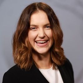 A woman in a dark blazer and white T-shirt with a broad smile