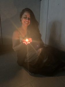 A woman in a Dark Sari sits on the floor holding a lit candle smiling