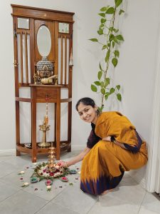 A woman in an Orange Sari is smiling whilst placing a tea light candle in a shrine 